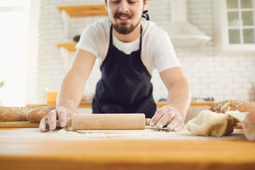 Baker male bearded man makes fresh bread dough at a table in the bakery kitchen.