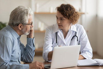 Young female professional doctor physician consulting old male patient, talking to senior adult man...