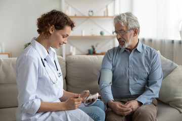Woman doctor cardiologist or physician checking high blood pressure examining old male patient...