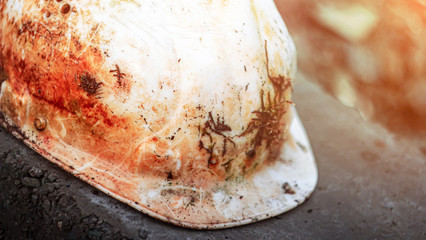 An old soiled white plastic safety helmet for an engineer or worker placed on a concrete block in a...