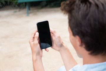 portrait behind of young man holding cellphone and looking at screen