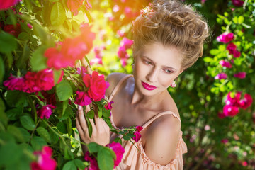 Beautiful portrait of blonde woman with retro hair done fair haired in bright pink roses. Empress style woman. Girl in the flower pink rose garden.
