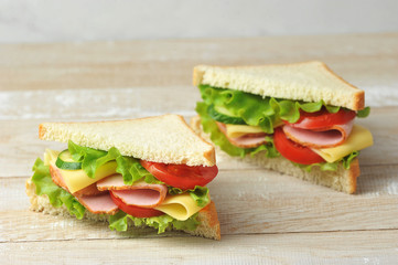 Ham and cheese sandwich on a light wooden background. Slices of fresh cucumber, tomato and salad are part of the sandwich filling. Close-up.