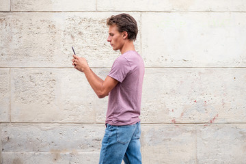 Side of young man walking by wall looking at mobile phone