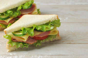 Sandwich with ham and cheese made of white bread. Light wooden background. Free space for text.