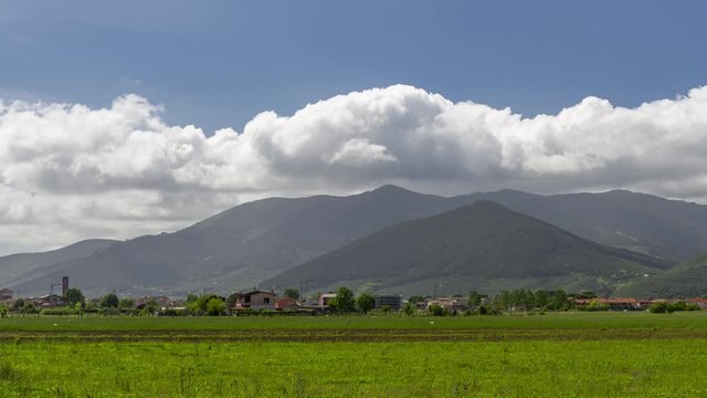 Hyperlapse of the Tuscan village of Bientina, Italy, seen from the surrounding countryside with Monte Pisano and Monte Serra in the background on a sunny day with white clouds in motion