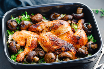 Top view of roasted chicken legs and breasts with fresh salad and mushrooms in black dish.