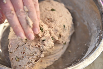 Close up of a baker kneading bread dough in a metal bowl. 
Handmade bread dough in a stainless steel bowl.