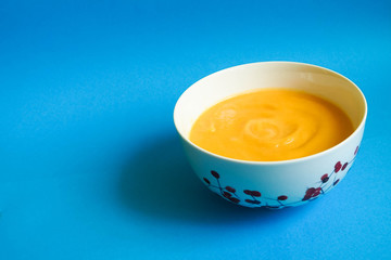 Orange soup puree of pumpkin, potatoes, carrots and cream in a white plate on a blue background.  Gluten-free baby soup
