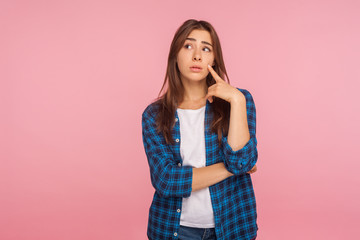 Need to think over difficult decision! Portrait of pensive girl in checkered shirt looking aside with doubtful thoughtful face, pondering intensely concentrating. indoor studio shot, pink background