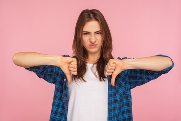 Don't like, bad quality! Portrait of disgruntled girl in checkered shirt gesturing thumbs down and...