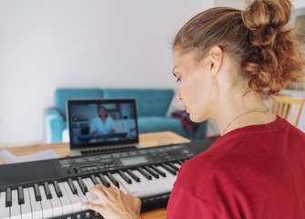 Young girl woman learns to play the piano with a teacher on a video conference from a laptop. The teacher on the screen explains on the Internet. Education video calls self education © olezzo