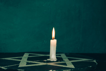 Close up one burning candles and the Star of David against on a green background wall.