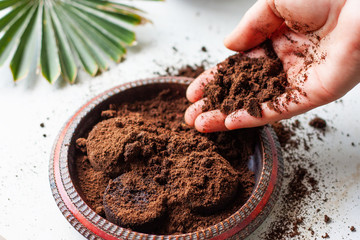 Woman's hand crumbles coffee grounds into wooden bowl. Coffee grounds used as a body scrub or...