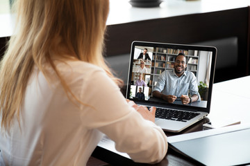 Back view of businesswoman sit at desk talk on video call with multiracial colleagues, woman...