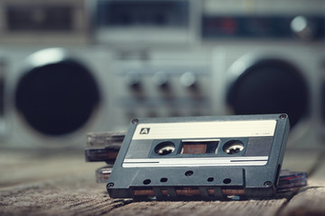 Retro compact cassette tape on the foreground lying on an old wooden table with a cassette recorder...