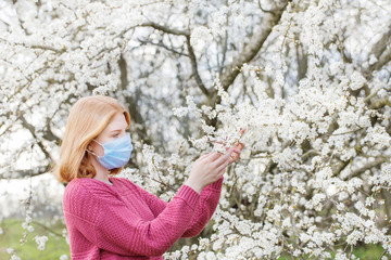 Happy teenager girl in medical mask in spring flowering garden. Concept of social distance and prevention of coronavirus.