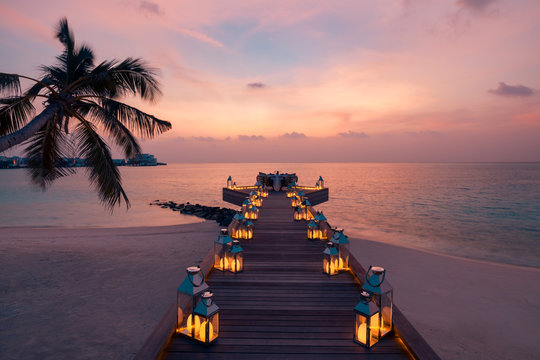 Romantic dinner on the beach with sunset, candles with palm leaves and sunset sky and sea. Amazing view, honeymoon or anniversary dinner landscape. Exotic island evening horizon, romance for a couple 
