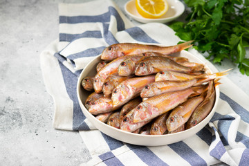 Black sea barabulka fish in a white ceramic bowl on a light gray kitchen table. A lot of fish red mullet. Black sea barabulka