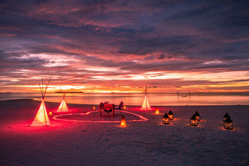 Romantic dinner with wine, candles and torches at ocean beach during wonderful sunset and flying birds couple. Honeymoon, proposal or wedding background concept.
