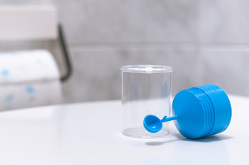 A stool sample container for fecal tests in the bathroom with a roll of toilet paper on the...