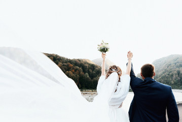 The bride and groom with a developing veil raise their hands up