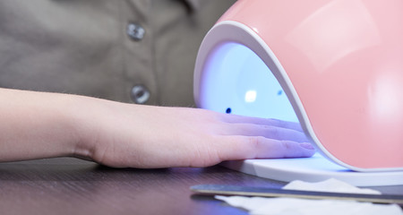 Gel Polish at home. Hand in a glowing UV lamp. The concept of hand care in self-isolation.