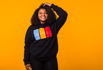 Youth street fashion concept - Confident sexy black woman in stylish sweatshirt having fun on yellow background with copyspace.