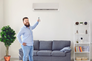 Fat funny man holding an air conditioning control panel at home. Air conditioner. - obrazy, fototapety, plakaty