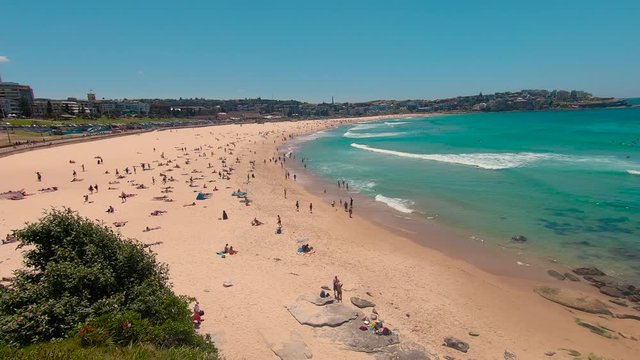 Bondi Beach Sydney holiday scene. Famous vacation spot in city, with beautiful ocean, sun, sea and sand. Tourists sunbathing on beach, with waves washing in. Australia. 4k.