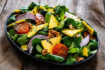 Fresh salad - blue cheese, cherry tomatoes, vegetables and walnuts on wooden background

