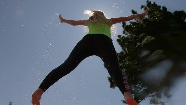 a young woman in a jump with a splash of water. athletic girl jumps up with flying jets of water against the background of summer mountains and sky. Sports and healthy lifestyle. Pretty fit girl