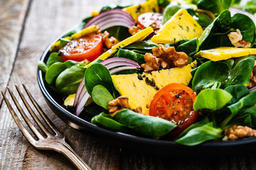 Fresh salad - blue cheese, cherry tomatoes, vegetables and walnuts on wooden background
