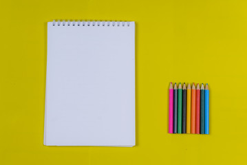 Empty notebook and  color pencils  on a yellow background