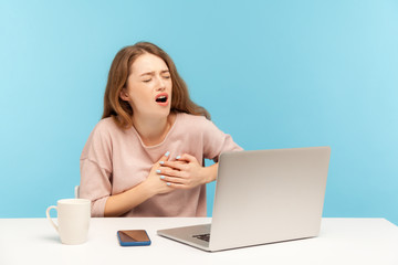 Stressful job. Fatigued ill woman employee sitting at workplace with laptop and holding painful chest, suffering heart attack, myocardial infarction. indoor studio shot isolated on blue background