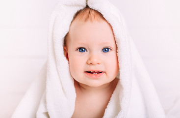 A cute baby with blue eyes wrapped in a white towel as the hood looks into the camera.