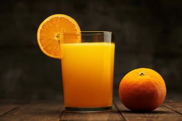 Fresh orange juice and fruits whole and sliced on a wooden table - natural and healthy food and drink. One glass of cocktail with a slice of fruit
