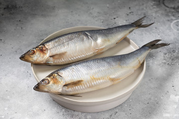 Herring on a white plate on a light gray table. Salted fish