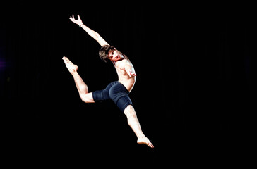 Modern ballet style male dancer performs on high lighted stage .