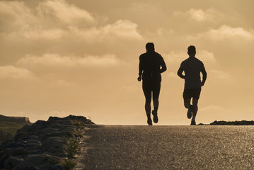 silhouettes of two joggers running on a rural street against vivid evening sky