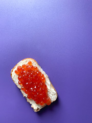Sandwich with butter and red salmon caviar. Toast white bread is spread with butter or soft cheese. Violet monophonic background for backgrounds.