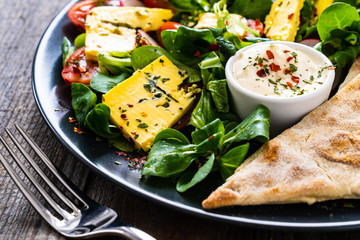 Fresh salad - blue cheese, cherry tomatoes, vegetables and homemade bread on wooden background 