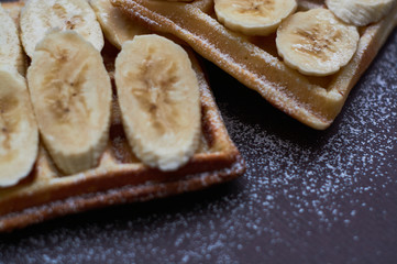 Fototapeta na wymiar Belgian waffles with banana and sugar powder on dark background.