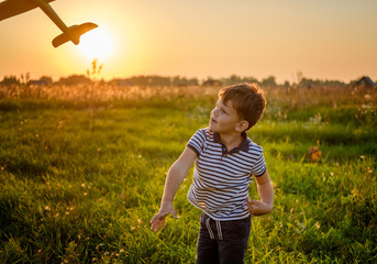 cute boy playing airplane on a summer evening against the sunset