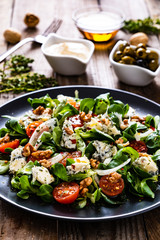 Fresh salad - blue cheese, cherry tomatoes, vegetables and walnuts on wooden background
