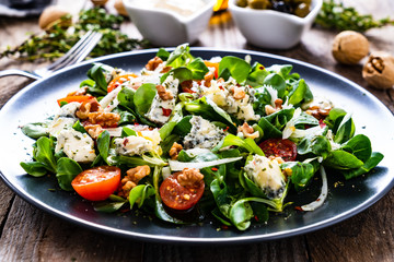 Fresh salad - blue cheese, cherry tomatoes, vegetables and walnuts on wooden background
