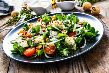 Fresh salad - blue cheese, cherry tomatoes, vegetables and walnuts on wooden background
