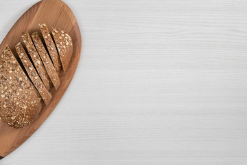 Sliced bread with seeds and flakes on wooden board on white background.