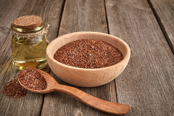 Flax seeds and a wooden spoon on a wooden table. Wooden bowl with bottle of oil. Healthy food and drink concept.