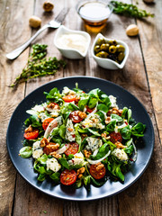 Fresh salad - blue cheese, cherry tomatoes, vegetables and walnuts on wooden background
